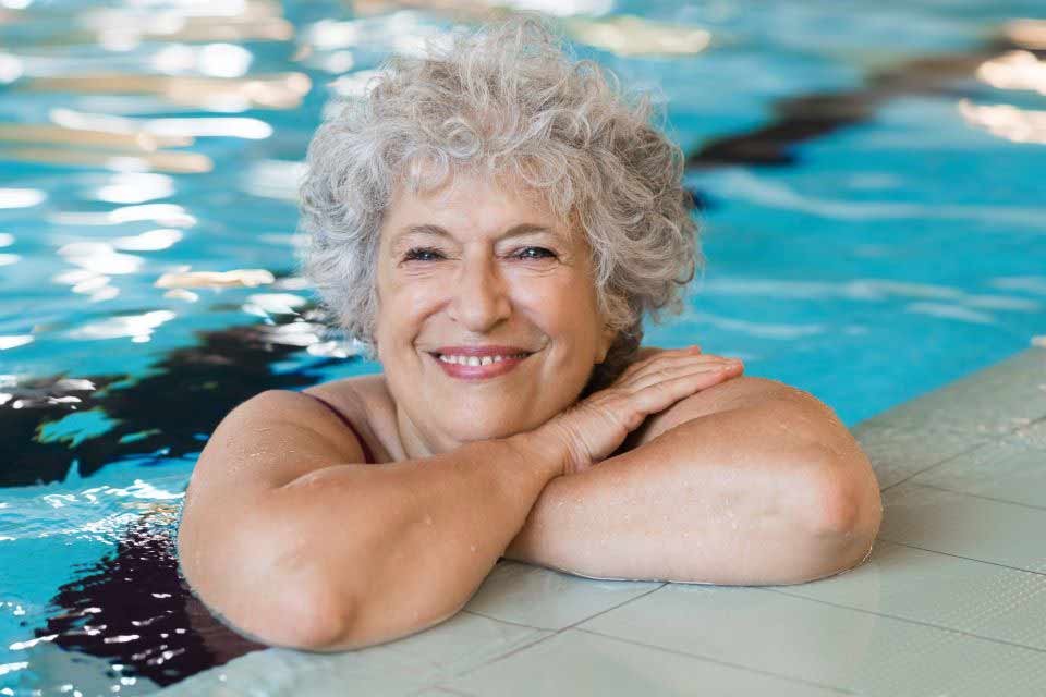 Elderly woman resting on the edge of a swimming pool.